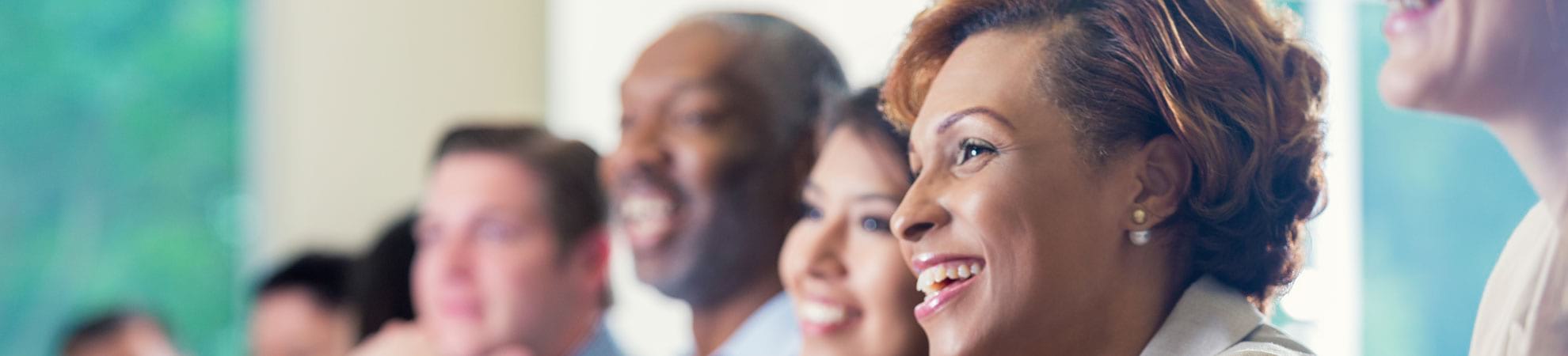 People smiling looking forward with woman in the foreground.