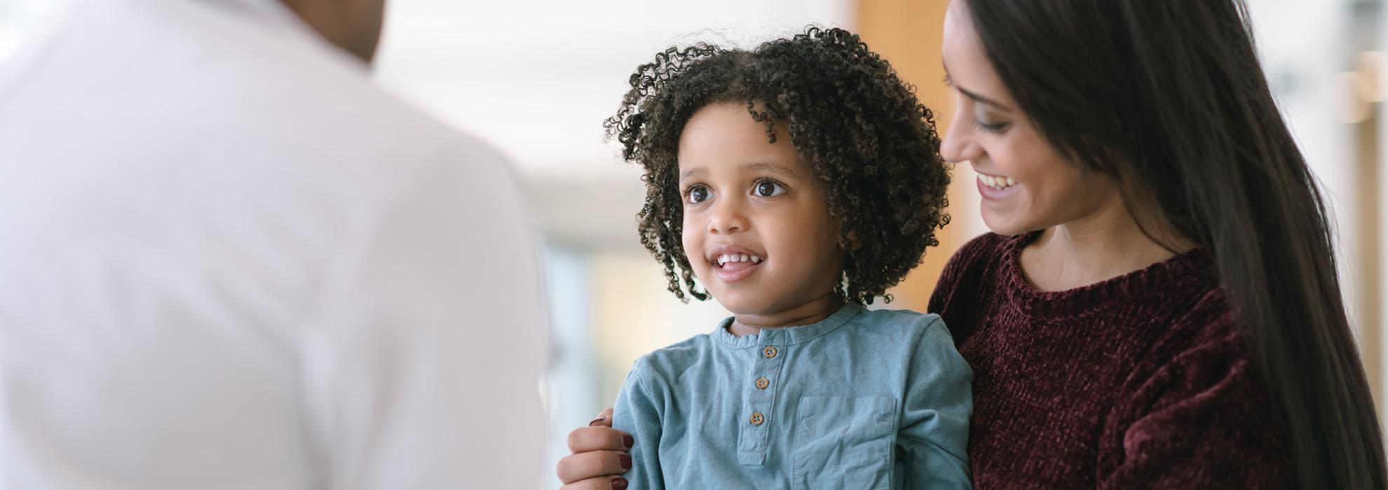 Woman holding a girl that's smiling at a doctor.