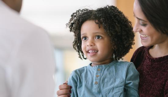 Woman holding a girl that's smiling at a doctor.